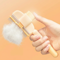 PawLunor Grooming Comb held in hand with fur being ejected, warm peach background